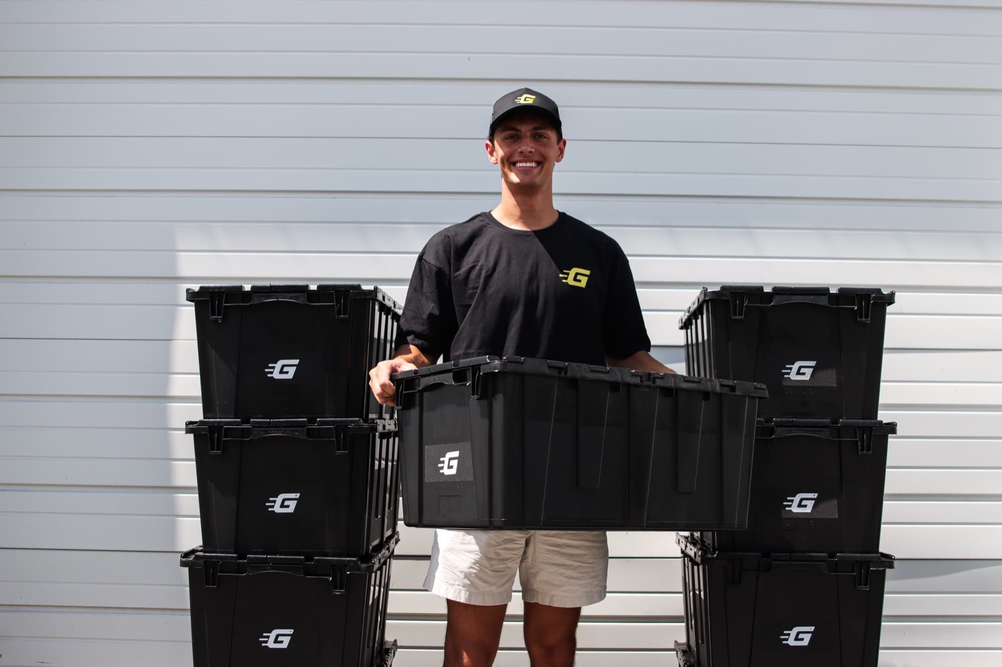 A Ghatt2Go team member carrying a black rental bin between two stacks of bins